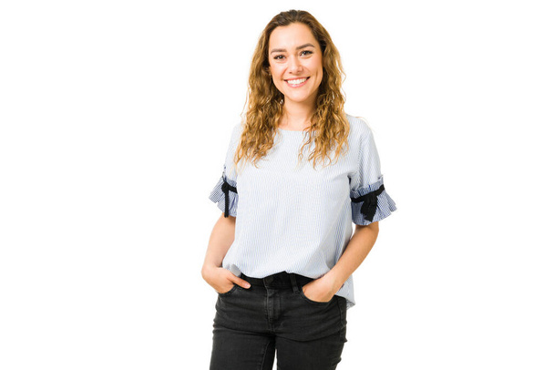 Cheerful young woman making eye contact with the hands on her pockets. Latin smiling woman posing against a white background - Фото, изображение