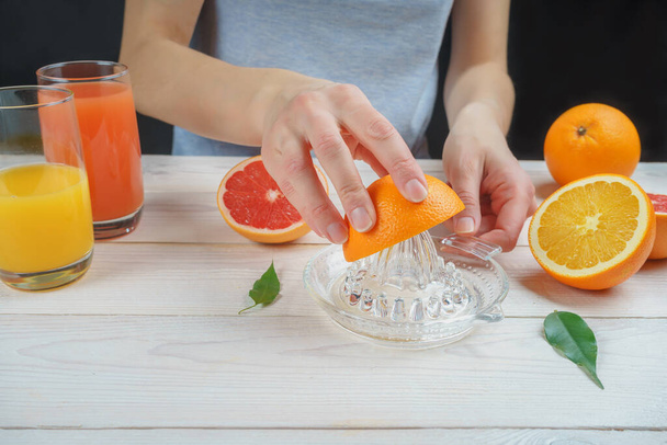 Young woman squeezes orange juice using a manual glass juicer. - Valokuva, kuva