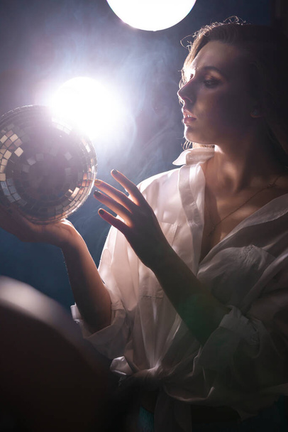 young woman in a club of smoke and soap bubbles holds a shiny disco ball in her hand - Fotó, kép