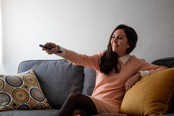 Молодая женщина включает телевизор и расслабляется - Фото, изображение