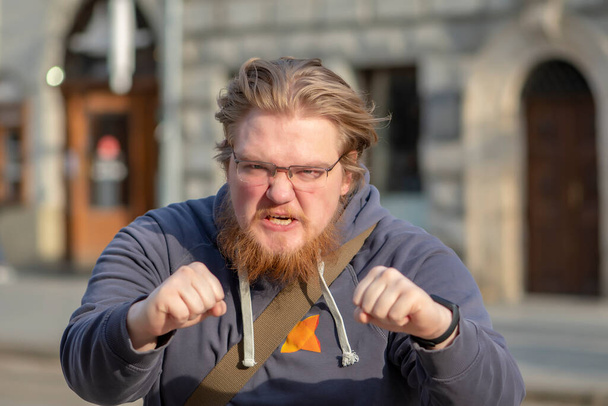 Straßenporträt eines 25-30-jährigen Mannes mit Brille und wütendem Gesichtsausdruck, der auf städtischem Hintergrund kämpfen will. - Foto, Bild