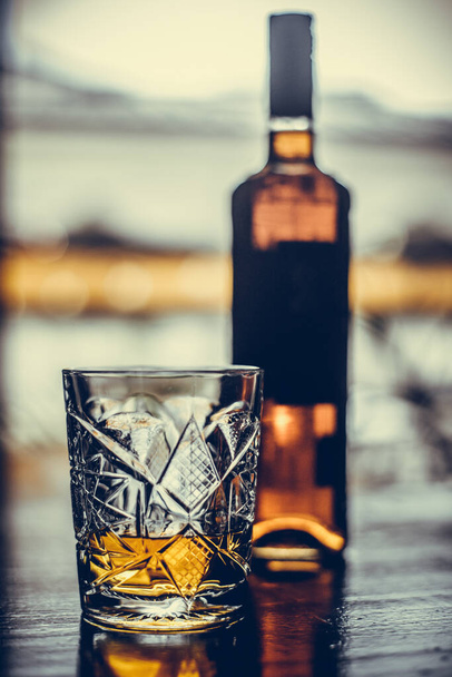 Colpo da vicino di un bicchiere di whisky e una bottiglia su una superficie di legno. - Foto, immagini