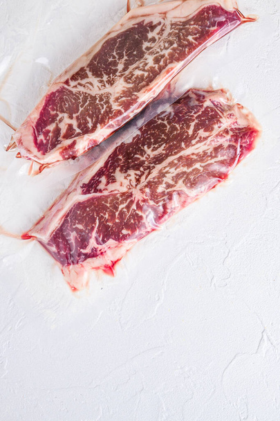 Bistecca superiore, carne di manzo biologica confezionata sottovuoto su sfondo bianco con texture in cemento, vista dall'alto con spazio per il testo - Foto, immagini