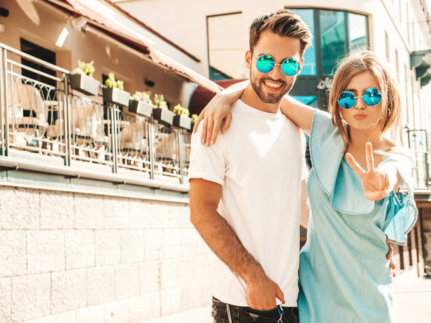 Portrait of smiling beautiful woman and her handsome boyfriend. Woman in casual summer jeans dress. Happy cheerful family. Female having fun. Couple posing on the street background in sunglasses - Photo, image