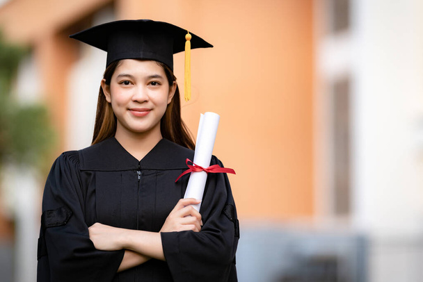 Uma jovem mulher asiática feliz universidade graduado em vestido de graduação e argamassa detém um certificado de grau celebra a realização da educação no campus universitário. Educação fotos stock - Foto, Imagem