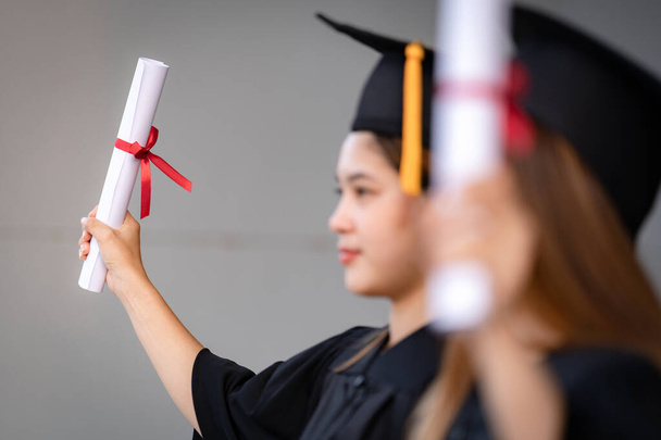A young happy Asian woman university graduate in graduation gown and mortarboard holds a degree certificate celebrates education achievement in the university campus.  Education stock photo - 写真・画像
