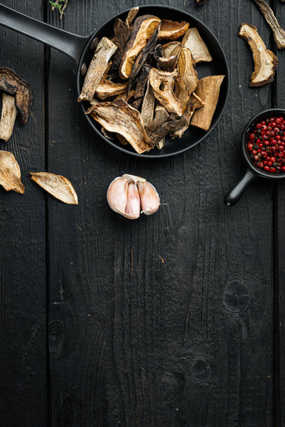 Set of dried mushrooms set in cast iron frying pan, on black wooden table background, top view flat lay , with space for text copyspace - Photo, Image