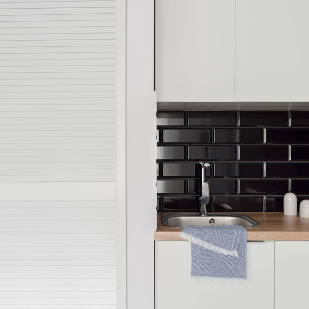 Close -up on small kitchen sink with black rectangular backsplash tiles next to white wardrobe - Foto, Imagen