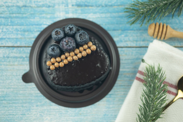 Свежий вкусный шоколадный торт форма сердца декор с ягодами на пластиковой коробке помещен на деревянный стол, вид сверху - Фото, изображение