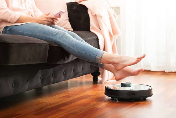 Seção do meio sem rosto de mulher jovem usando aspirador automático para limpar o chão, controlando robô doméstico máquina inteligente - Foto, Imagem