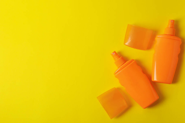 Помаранчеві пляшки сонцезахисного крему на жовтому тлі
 - Фото, зображення