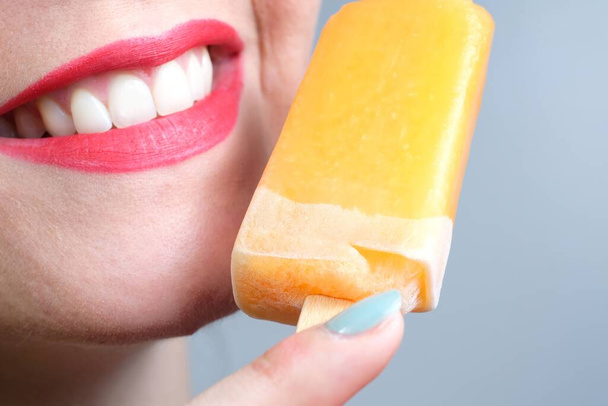 Close up of a smiling woman with sensual red lips and orange ice cream   - Foto, Imagem