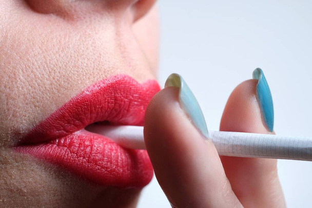 Şehvetli kırmızı dudakları ve sigara içen yeşil tırnaklı bir kadının yakın çekimi. - Fotoğraf, Görsel