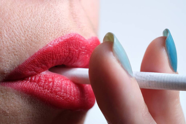 Şehvetli kırmızı dudakları ve sigara içen yeşil tırnaklı bir kadının yakın çekimi. - Fotoğraf, Görsel