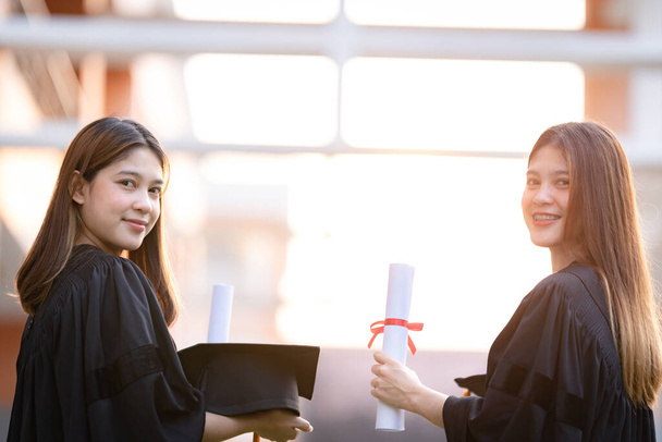 若い幸せなアジアの女性の大学卒業生は卒業生のガウンとモルタルボードは、大学のキャンパスで教育の成果を祝う学位証明書を保持します。教育ストックフォト - 写真・画像
