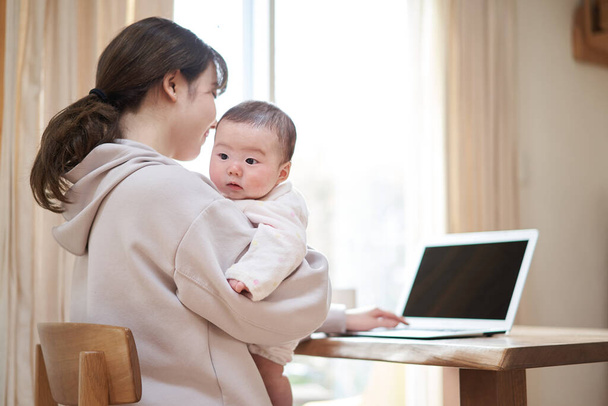 Asiatique maman de travail tandis que babysitting son bébé - Photo, image