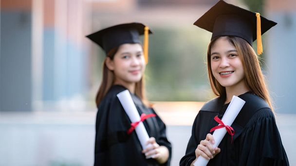 Молодые счастливые азиатские женщины-выпускницы университетов в выпускных платьях и минометах имеют диплом об образовании в университетском городке. Фондовое фото - Фото, изображение