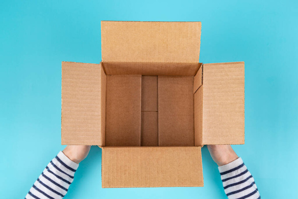 Female hands with empty open cardboard box on light blue background. Top view - 写真・画像