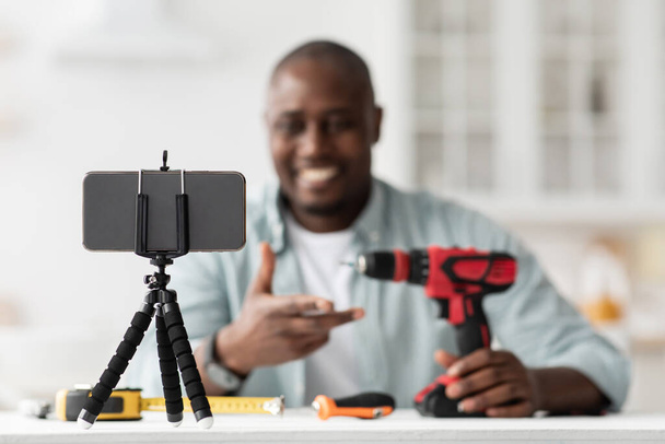 Carpenter blogger recording video review of instruments on phone, showing modern electric drill, selective focus - Photo, image