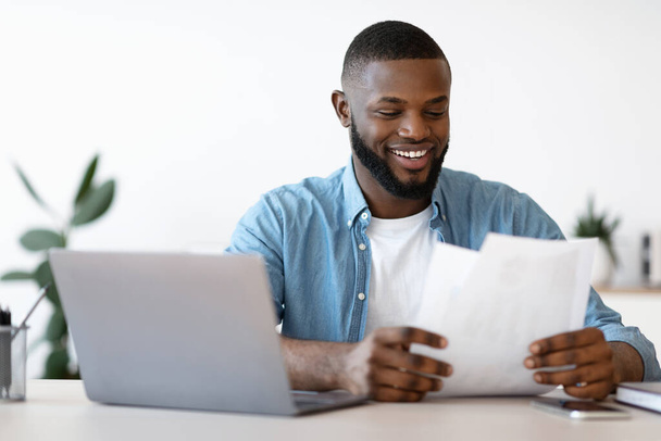 Веселий молодий чорний підприємець працює з паперами в сучасному офісі
 - Фото, зображення