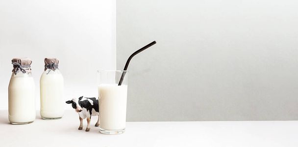 Des bouteilles de lait frais, une figurine de vache et un verre de lait sur fond gris clair. Nature morte minimaliste du lait, espace de copie. - Photo, image