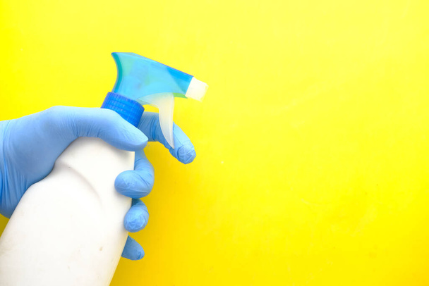hand in blue rubber gloves holding spray bottle on yellow background  - Foto, Bild