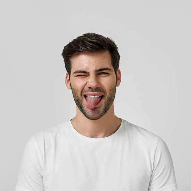 Man in a white t-shirt showing his tongue - Zdjęcie, obraz