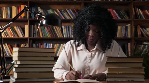 Mujer afroamericana escribe en cuaderno en biblioteca pública - Metraje, vídeo