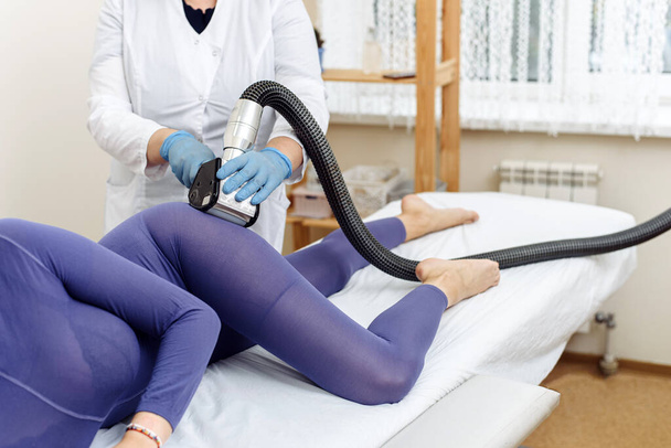 Косметолог робить LPG масаж попою молодої жінки в фіолетовому костюмі. Лімфодренажний масаж. Лікування схуднення
 - Фото, зображення
