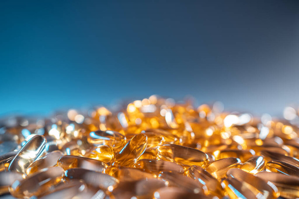 handful of golden fish oil capsules omega 3 vitamins on blue background - Фото, зображення