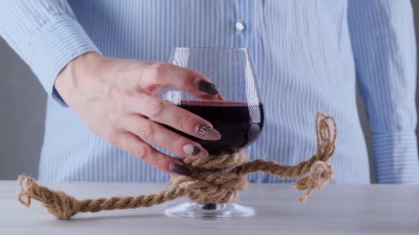 θηλυκό χέρι κρατώντας ποτήρι κρασί είναι δεμένο με ένα σχοινί γιούτα. Η έννοια της εξάρτησης από το αλκοόλ. - Πλάνα, βίντεο