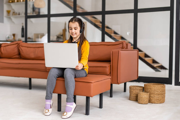 Smart Little Girl Does Homework in Her Living Room. Shes Sitting and Uses Laptop. - Foto, Bild