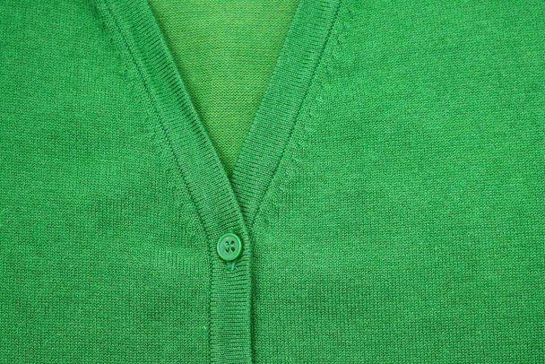 Часть зелёного свитера с зелёной кнопкой. Зеленый вязаный фон с кнопкой.  - Фото, изображение