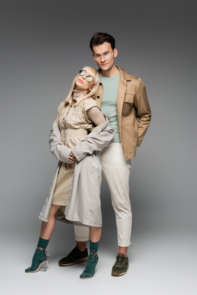 longitud completa de la pareja de moda posando de pie sobre gris - Foto, imagen