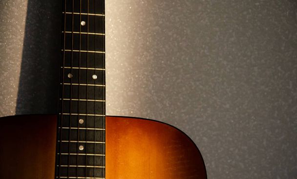 Fretboard de guitare focus sélectif avec cordes en rayon de soleil sur fond gris flou. Concept musical. Texture du cou de guitare avec espace de copie. Surface en tissu gris. Le processus créatif. - Photo, image