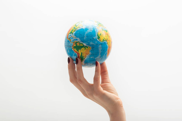 Globe at the tip of woman's fingers. Female hand holds globe. World in human hands. White background. - Photo, Image