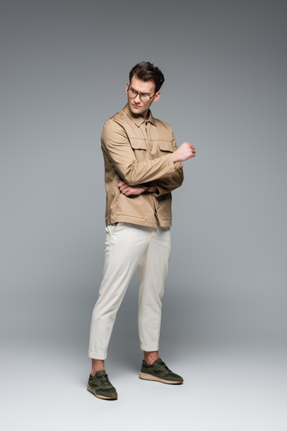 full length of trendy man in stylish outfit posing on grey - Foto, imagen