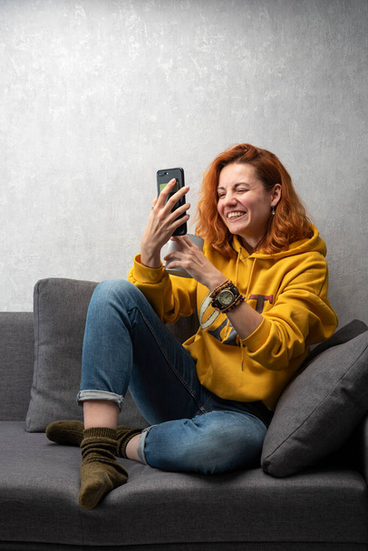 Cheerful young girl sits on the sofa and shoots stories. Chatting video call - Photo, Image