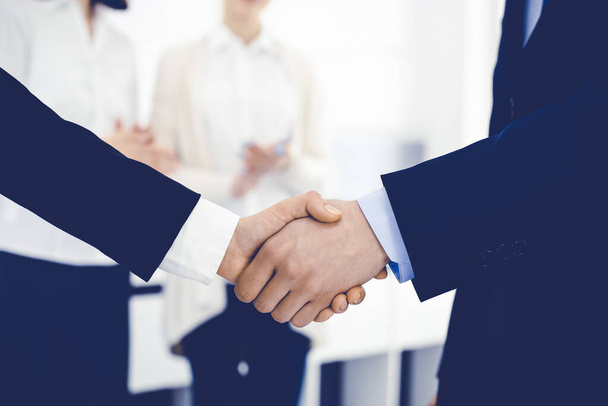 Businessman and woman shaking hands with colleagues at the background. Handshake at meeting in office. Concept of success in business - Фото, зображення