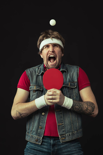 Joven caucásico divertido hombre jugando ping pong aislado sobre fondo negro. - Foto, Imagen
