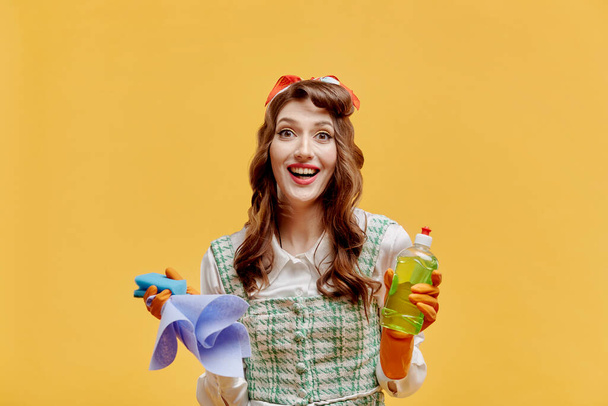 Happy cleaning woman with cleaning tools in the house. Yellow background. - Foto, imagen