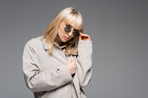 young fashionable woman adjusting sunglasses isolated on grey - Fotografie, Obrázek