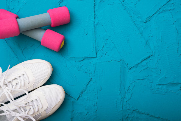 fitness at home - white sneakers and dumbbells lie on a textured background - Foto, imagen