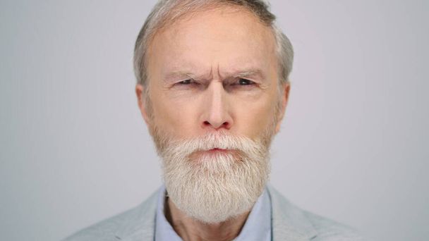Serious man squinting eyes in studio. Senior gentleman looking camera indoors. - Photo, Image