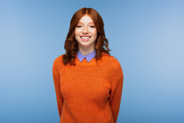 happy redhead woman in orange sweater isolated on blue - Foto, afbeelding
