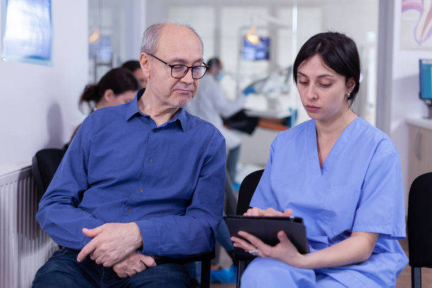 Infermiera prendere appunti su tablet pc discutendo con il paziente anziano in studio dentistico - Foto, immagini