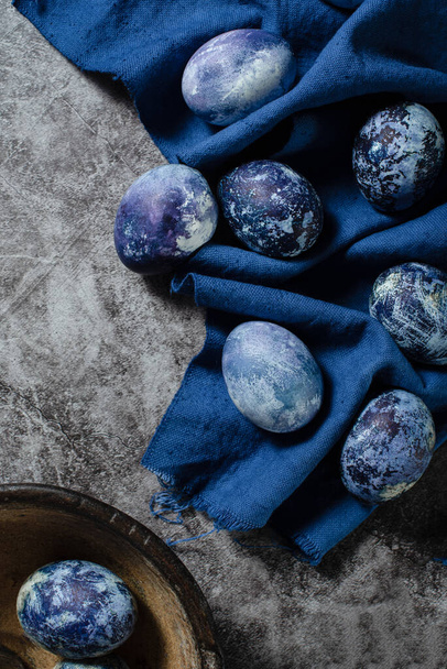 Los huevos de Pascua yacen sobre una toalla azul sobre un fondo de hormigón. huevos para colorear para Pascua con tinte natural de jugo de arándanos. - Foto, Imagen