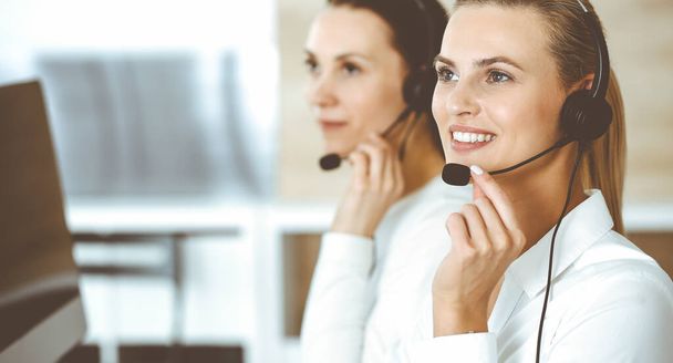 Blond female customer service representative and her colleague are consulting clients online using headset. Call center and business people concept - Φωτογραφία, εικόνα