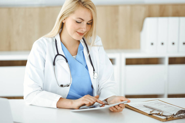 Женщина-врач, стоящая в больнице или клинике и использующая планшетный компьютер. Данные и лучший сервис в медицине и здравоохранении - Фото, изображение