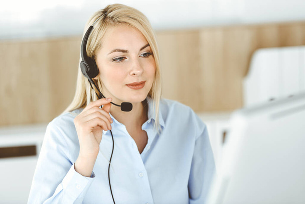 Blonde business woman sitting and communicated by headset in call center office. Concept of telesales business or home office occupation - Фото, изображение